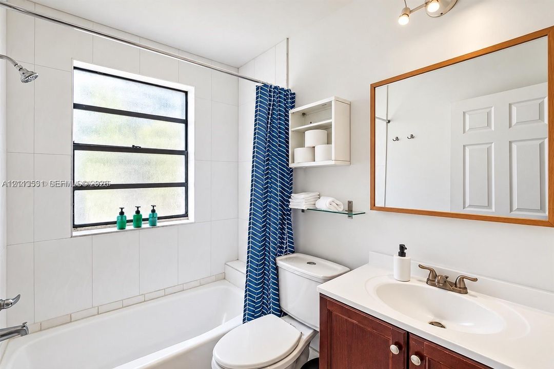 Bathroom featuring a tub with white tile surround, vanity with an integrated sink, framed wall mirror, glass shelving, and built-in wall cabinetry