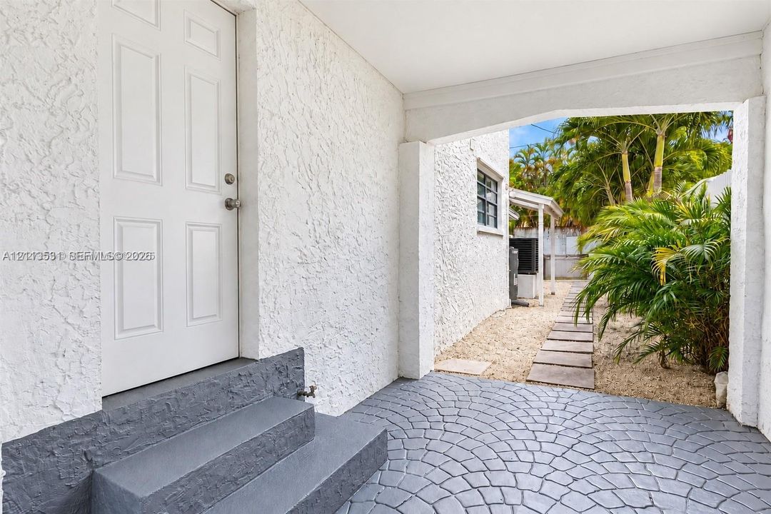 Covered entryway featuring a six-panel door, textured stucco exterior, decorative stone-patterned concrete flooring, and concrete step