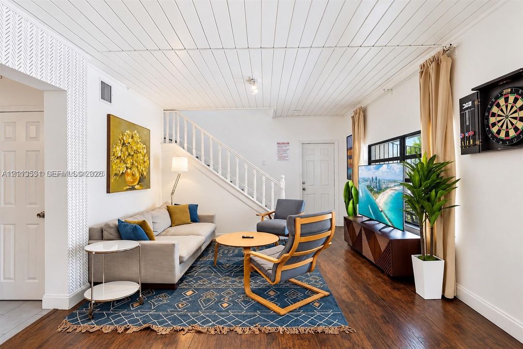 Living space featuring wood-finish flooring, a white tongue-and-groove plank ceiling, a staircase with white vertical railings, and a decorative textured accent wall
