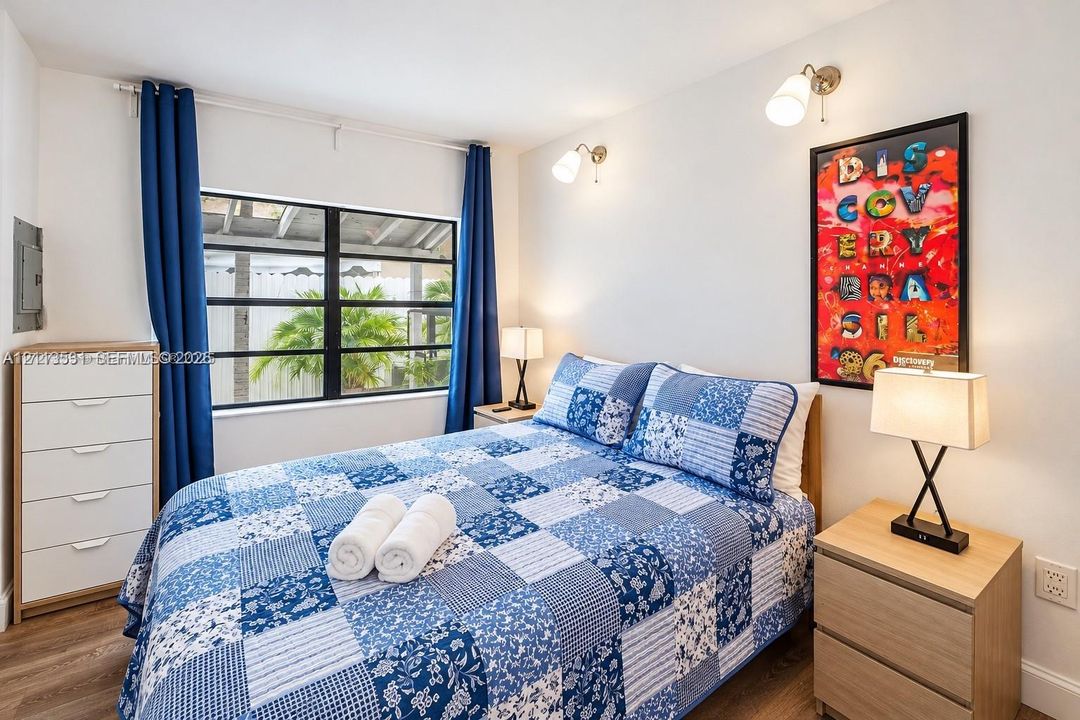 Bedroom featuring wood-finish flooring, large window with black framing, and two dual-arm adjustable wall sconces