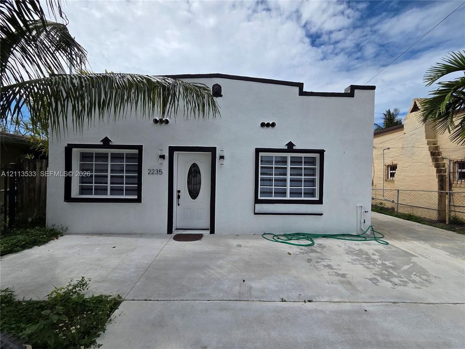 Stucco exterior with mission-style parapet, high-contrast window trim, single-entry door with oval glass insert, and concrete driveway