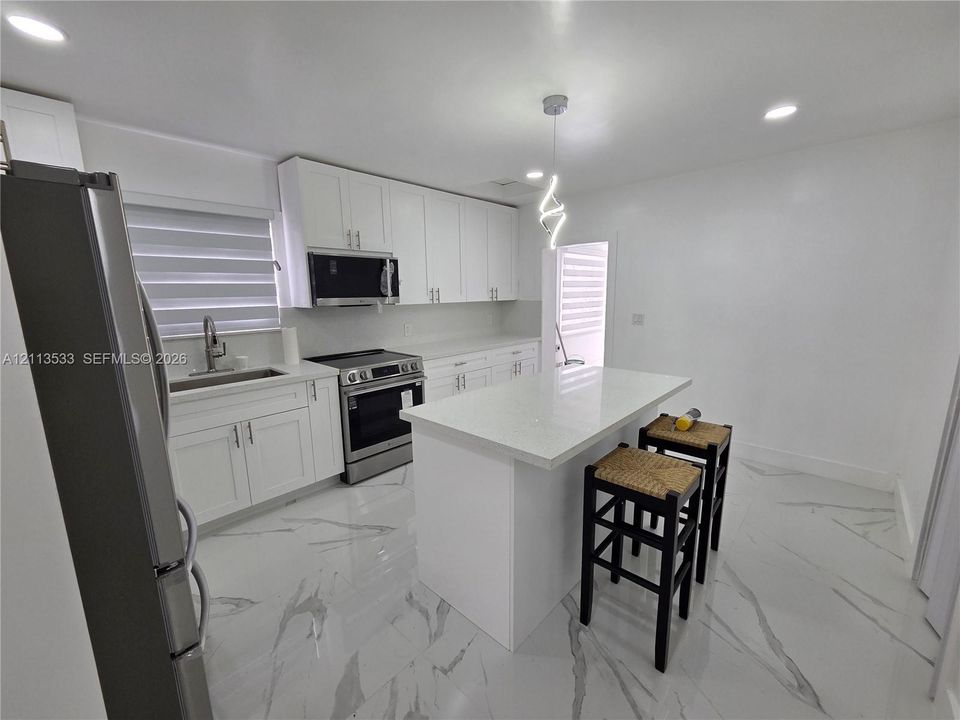 Kitchen featuring white shaker-style cabinetry, a central island with a solid surface countertop, stainless steel appliances, and large-format porcelain tile flooring with marble-style veining