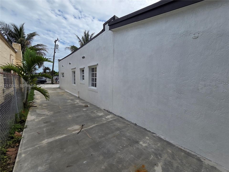 White stucco exterior featuring multi-pane windows, dark roof trim, and an expansive concrete side apron