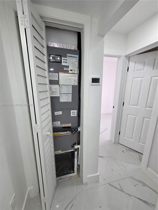Utility closet featuring a louvered bifold door, tile flooring, and wall-mounted digital thermostat