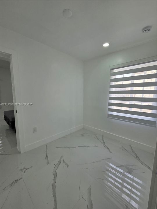Interior room featuring large-format tile flooring with marble-style veining, recessed lighting, and a window equipped with striped dual-layer roller shades