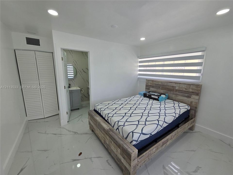Large-format polished tile flooring, recessed ceiling lighting, louvered-style closet doors, and adjustable dual-layer window treatments