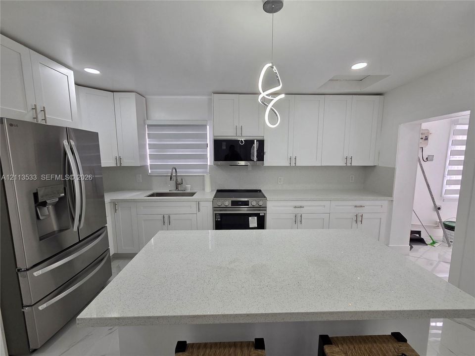 Kitchen featuring white cabinetry, quartz countertops, stainless steel appliances, a central island, and modern pendant lighting