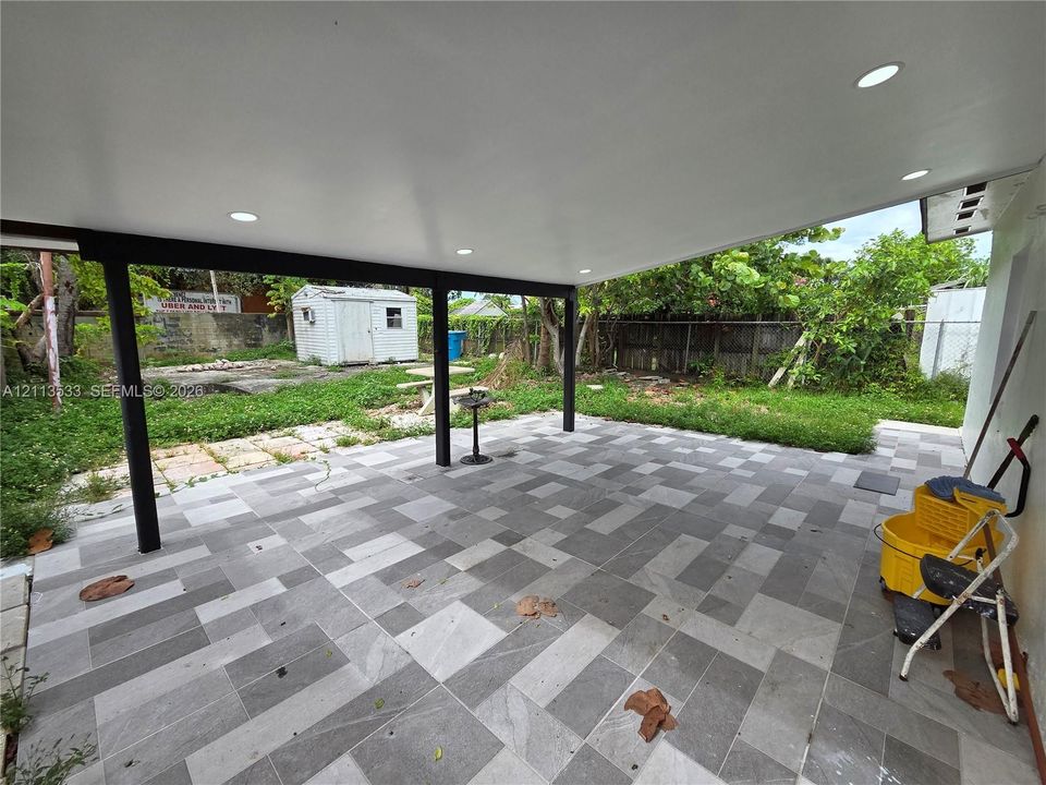 Covered patio featuring multi-toned tile flooring, recessed lighting, and black structural support columns