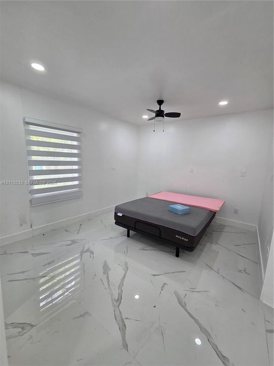 Large-format stone-style tile flooring, recessed ceiling lighting, central ceiling fan, and horizontal window shades