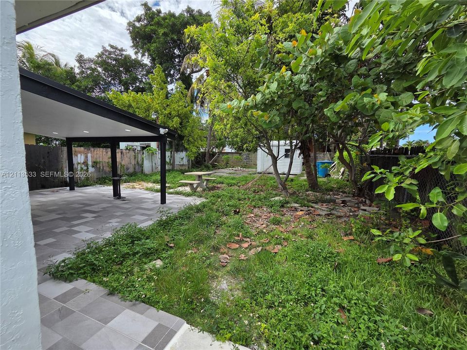 Covered patio featuring large-format ceramic tile flooring and recessed lighting, accompanied by mature trees and a fenced perimeter