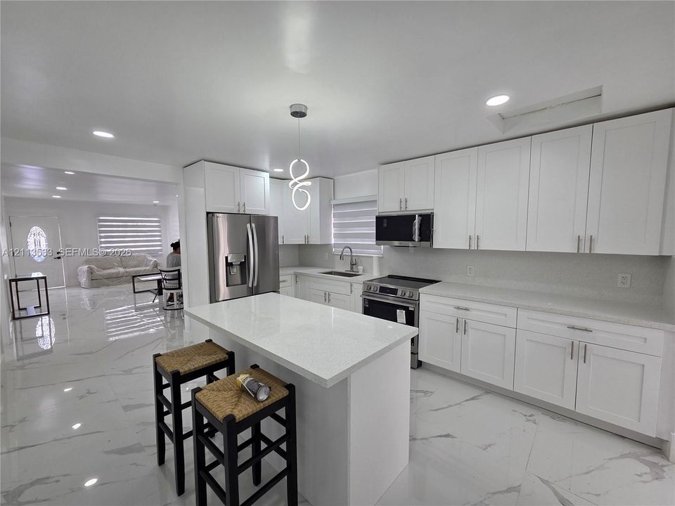 Kitchen featuring white cabinetry, solid-surface countertops, center island, stainless steel appliances, and large-format tile flooring