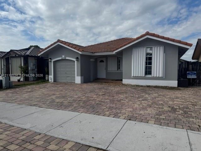 Single-story residence featuring a tile roof, gray exterior finish, attached one-car garage, and a decorative paver driveway