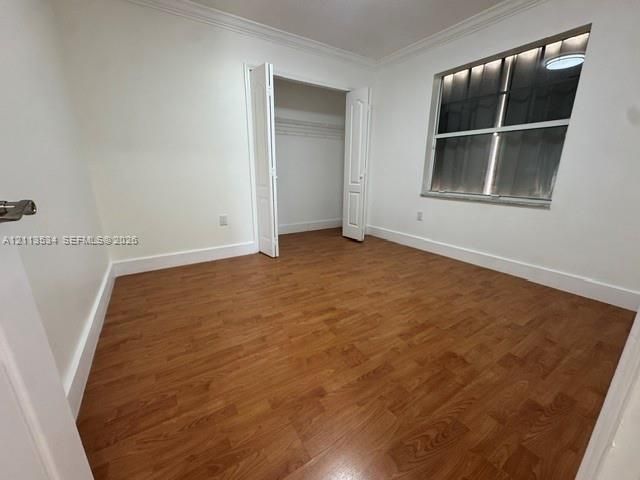 Room featuring wood-finish flooring, crown molding, and a closet with bifold doors