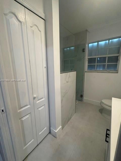 Bathroom featuring a walk-in shower with large-format tile surround, bi-fold closet doors, grid-pattern window, and tile flooring