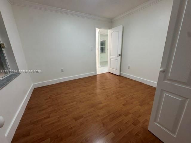 Room featuring wood-finish flooring, crown molding, and a solid-core paneled interior door