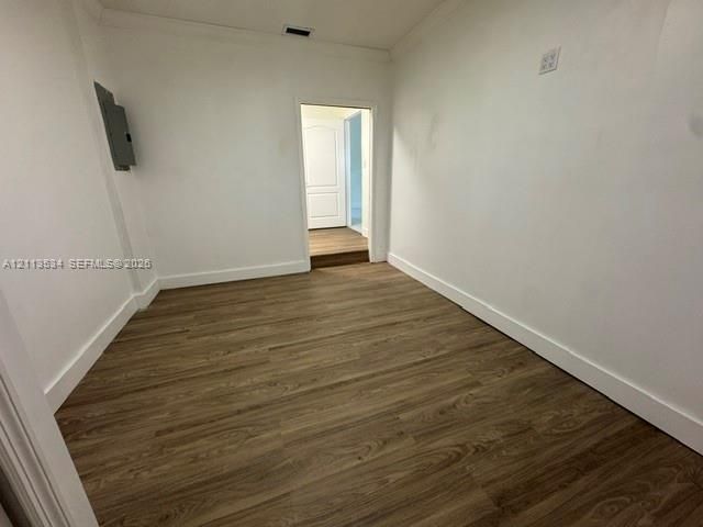 Interior room featuring wood-finish flooring, crisp white walls, crown molding, and a solid-core interior door