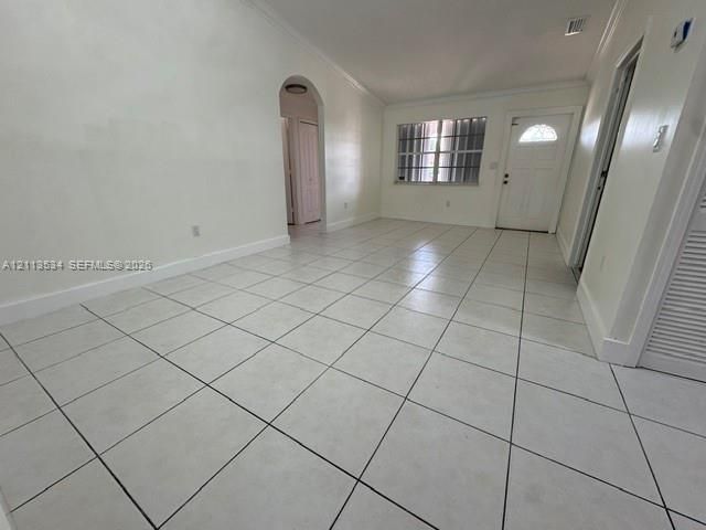 Neutral-toned ceramic tile flooring, arched architectural passage, multi-pane window, and white paneled entry door