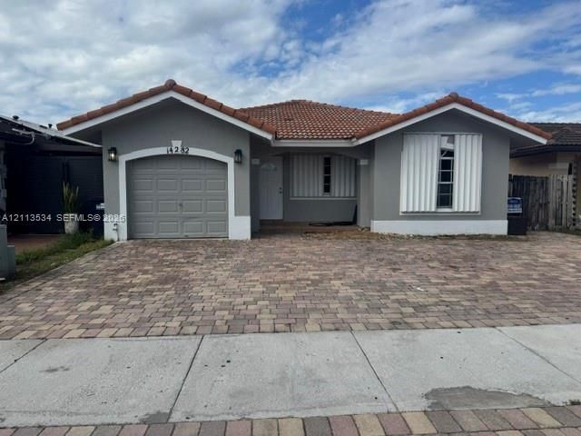 Single-story exterior featuring a clay tile roof, paver driveway, single-car garage, and shuttered windows