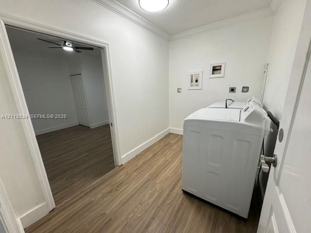 Laundry room featuring wood-finish flooring, white walls, crown molding, and a ceiling-mounted light fixture