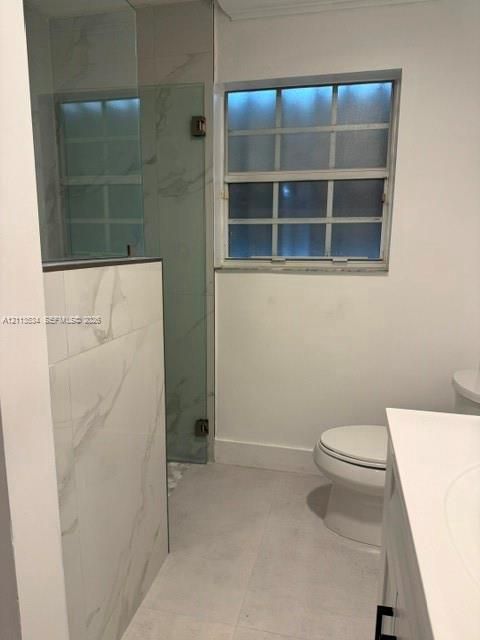 Full bathroom featuring large-format tile flooring, shower enclosure with floor-to-ceiling stone-patterned wall tile, glass pivot door, and vanity with integrated sink