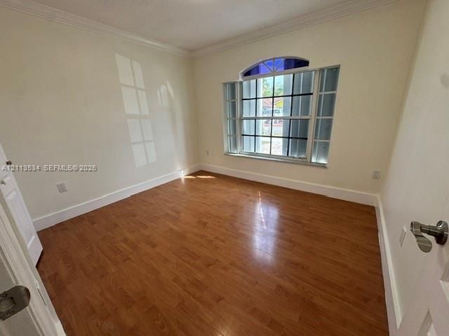 Interior room featuring wood-finish flooring, crown molding, and a multi-pane window with an arched transom