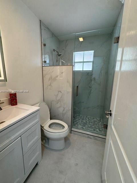 Walk-in shower with stone-patterned tile surround, frameless glass enclosure, pebble-tile flooring, and white cabinetry with integrated sink