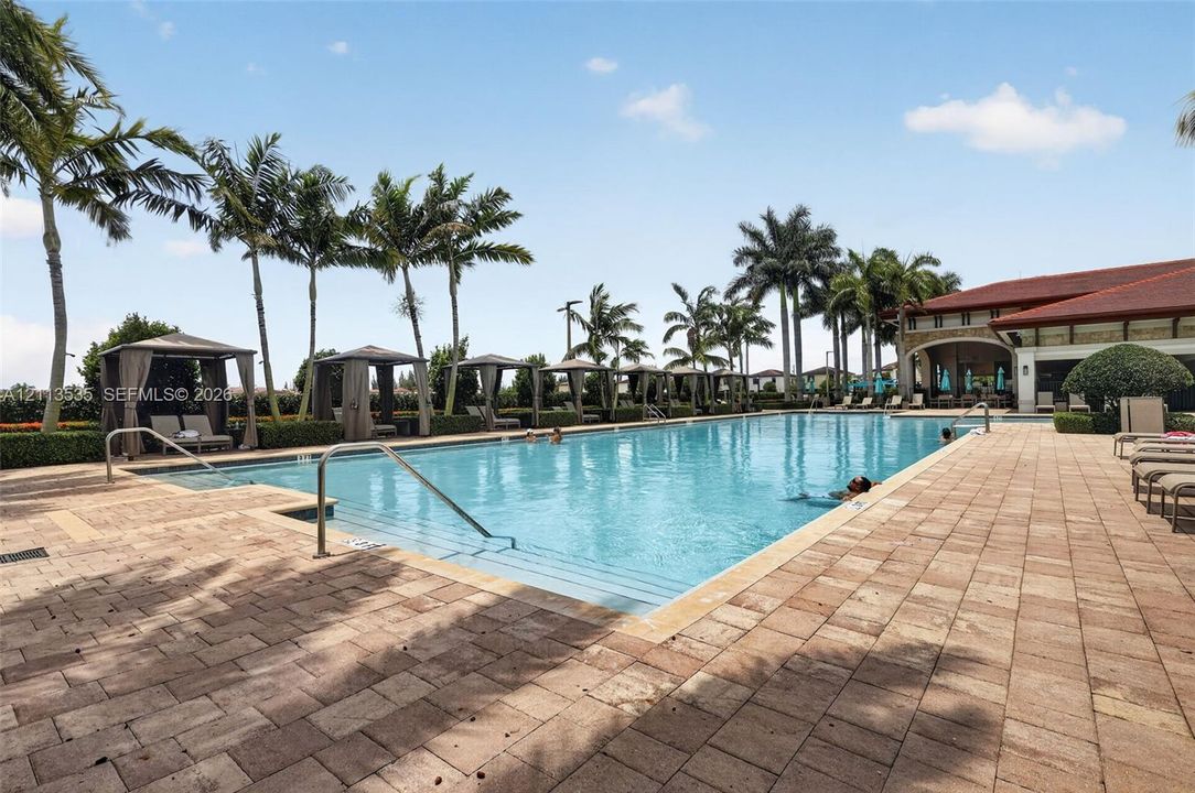 Swimming pool with paver decking, cabanas, and mature palm trees