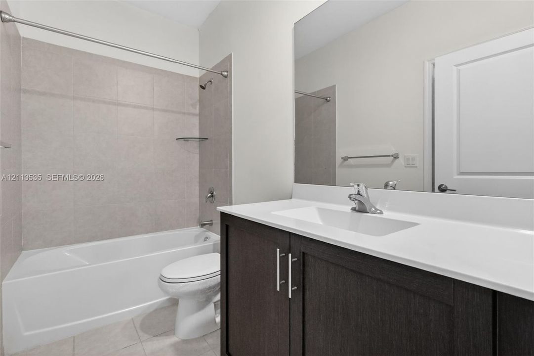 First Floor Bathroom featuring a dark wood-finish vanity with a white countertop, large wall-mounted mirror, and a tub-shower combination with full-height tile surround