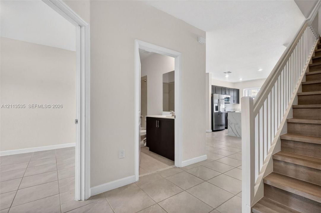 Staircase with wood-finish treads and white balusters, ceramic tile flooring, kitchen cabinetry with stone-surface island,
