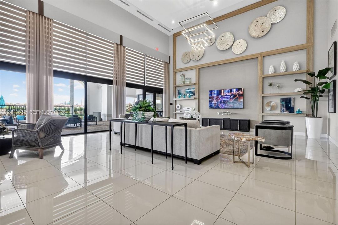 High-ceiling interior featuring expansive floor-to-ceiling windows, polished oversized tile flooring, built-in light-wood shelving, and a tiered geometric chandelier