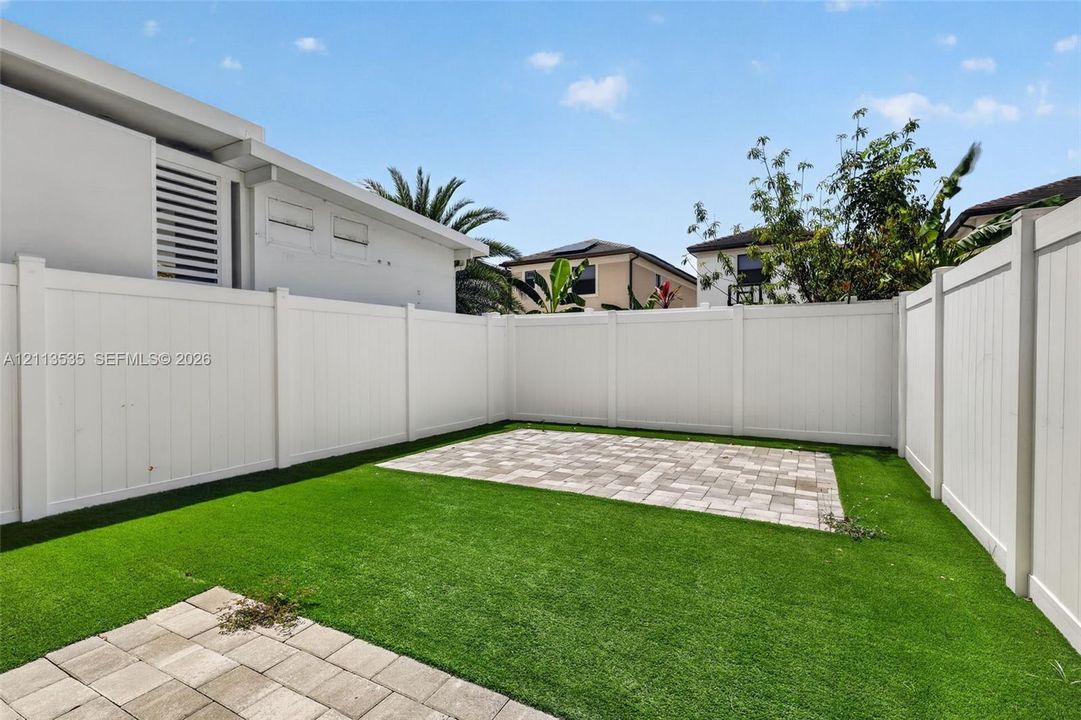 Enclosed yard featuring white privacy fencing, artificial turf lawn, and rectangular stone-paver hardscaping