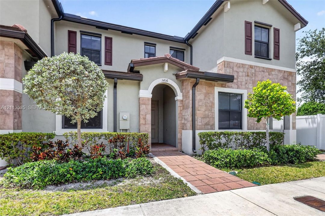 Two-story residence with a stucco exterior, stone facade accents, decorative window shutters, arched entryway, and paver walkway