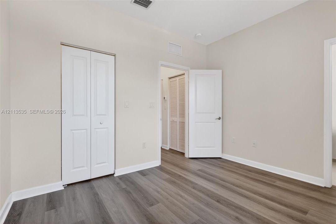 Room featuring wood-finish flooring, white panel doors, and a double-door closet with white finish