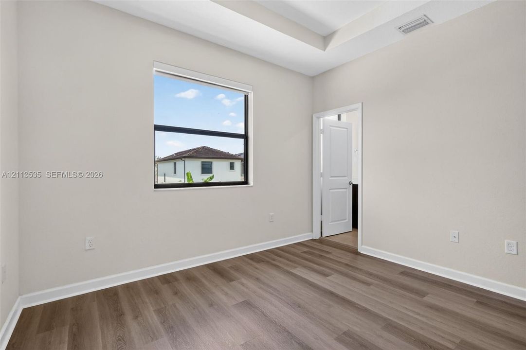 Room featuring a tray ceiling, wood-finish flooring, and a single-hung window with a dark frame