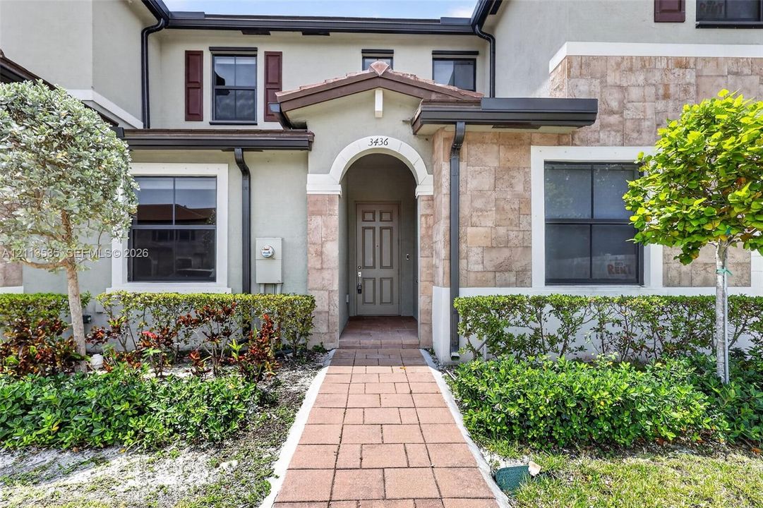 Exterior facade featuring a stone veneer entryway, arched doorway, paneled front door, and tiled walkway