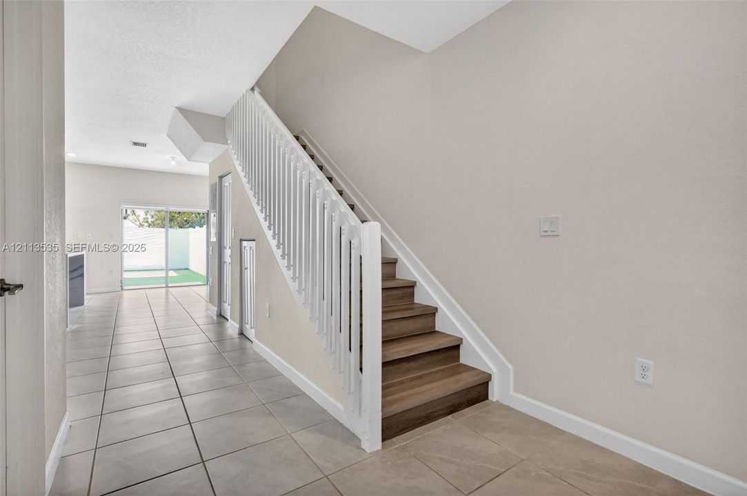 Staircase featuring wood-finish treads and white spindle railings, complemented by neutral tile flooring