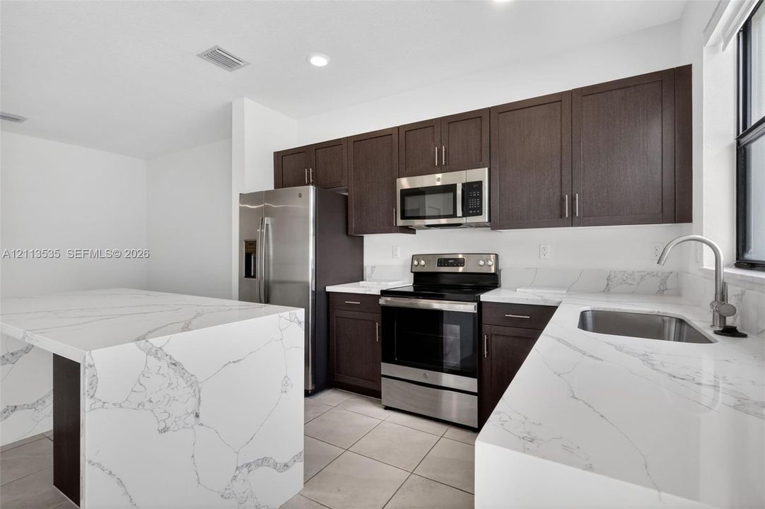 Kitchen featuring dark-toned cabinetry, waterfall-edge stone countertops, stainless steel appliances, and tile flooring