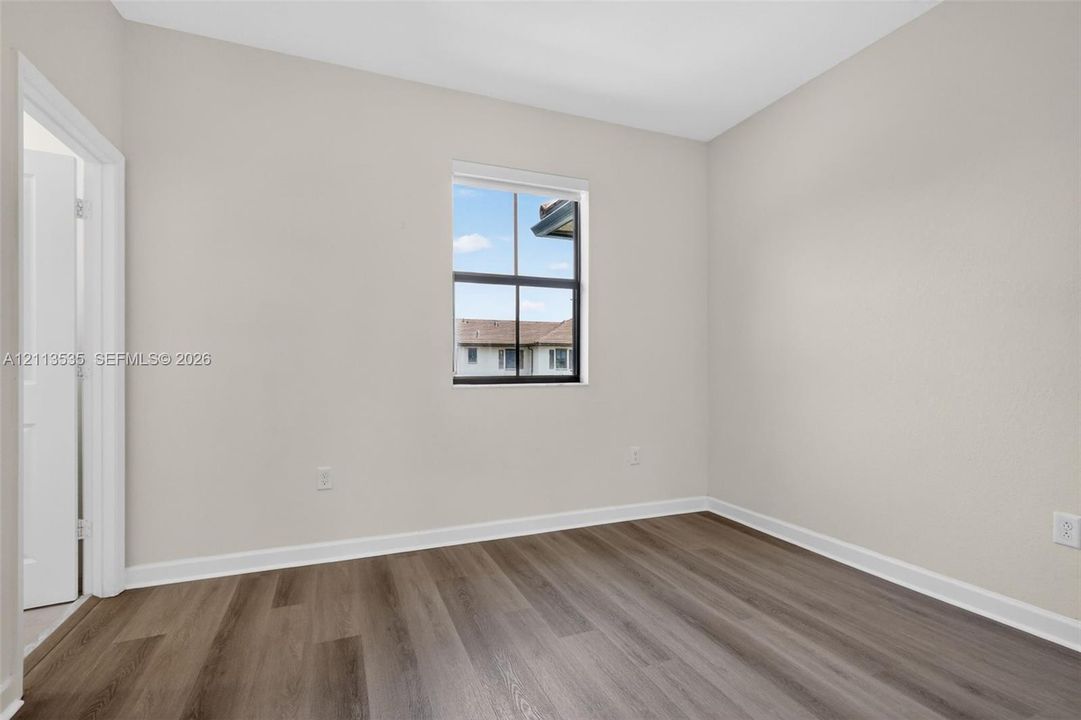 Neutral interior featuring wood-finish flooring, a single-hung window with a dark frame, and a hinged door