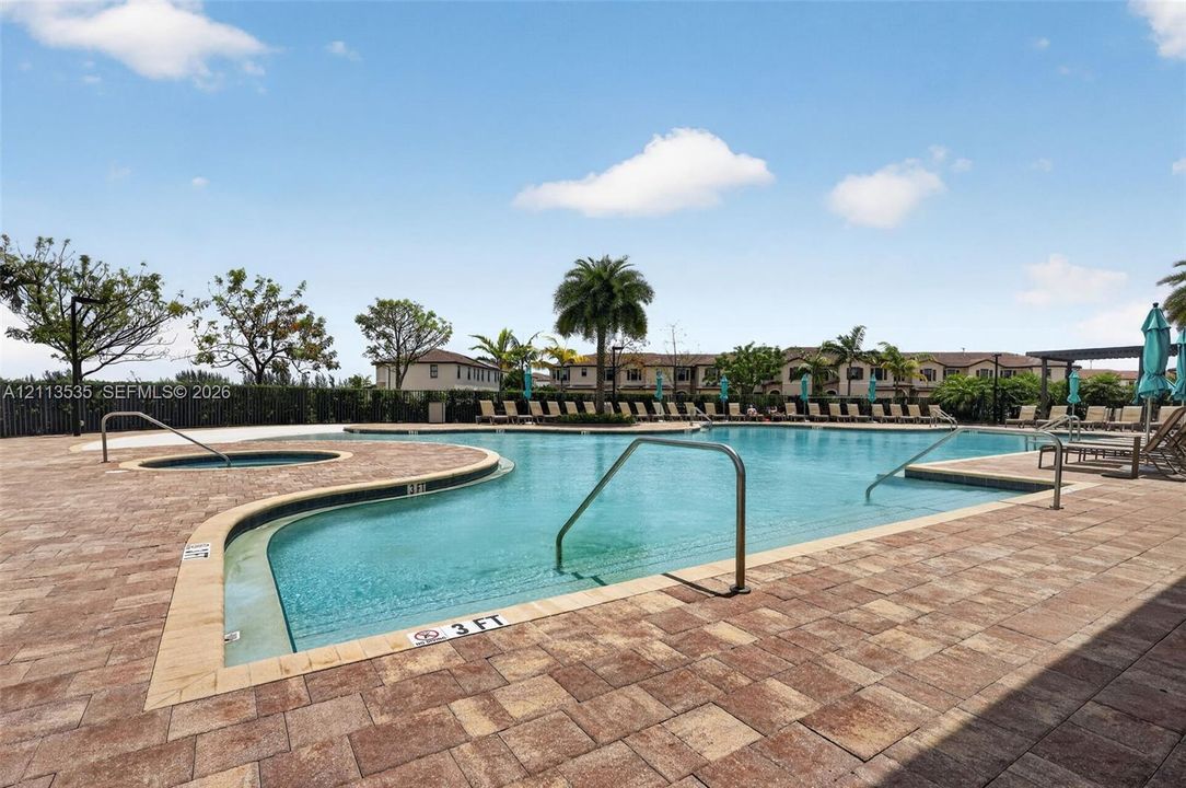 Swimming pool with an attached spa, featuring a paver stone deck and metal entry railings