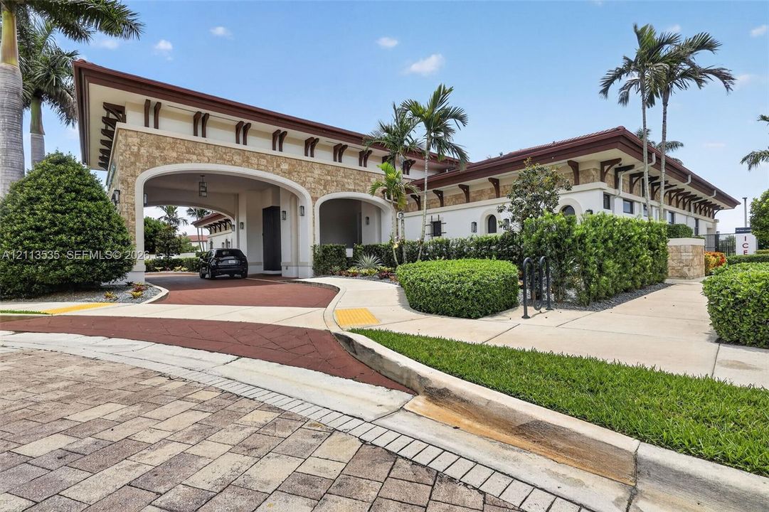 Exterior facade featuring decorative stone masonry, arched porte-cochère, exposed rafter tails, and a paved motor court