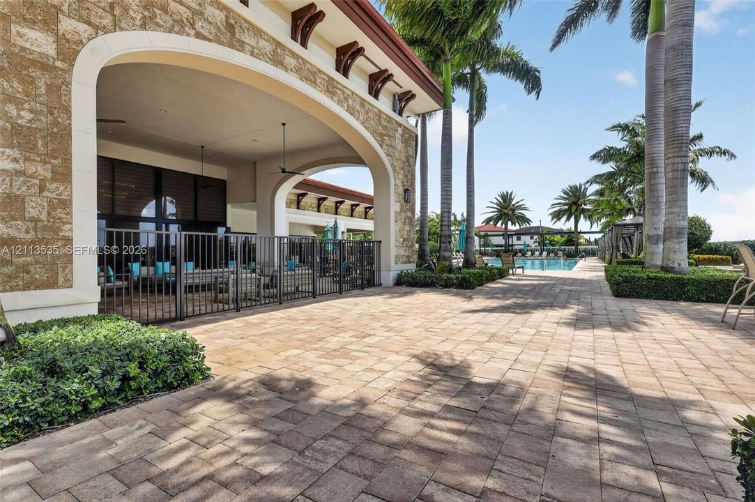 Covered patio featuring stone masonry, arched structural openings, paver hardscaping, metal perimeter fencing, and mature palm trees