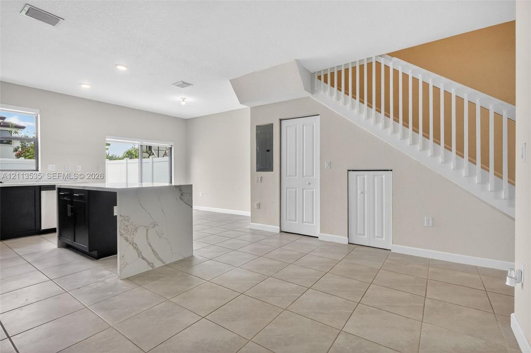 Open-concept interior featuring large-format tile flooring, a kitchen island with a stone-finish waterfall countertop, recessed lighting, and a staircase with white balusters