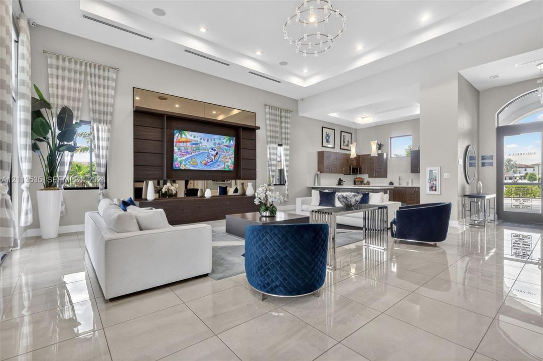 Open-concept living area featuring large-format tile flooring, tray ceilings with recessed lighting, a statement chandelier, and a custom built-in dark wood media wall with integrated shelving