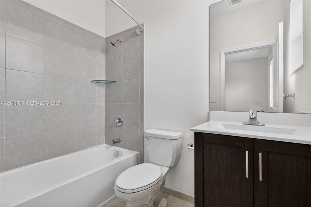 Bathroom featuring a dark wood-finish vanity, a white countertop with an integrated rectangular basin, a large-format mirror, and a tub-shower combination with full-height tile surrounds