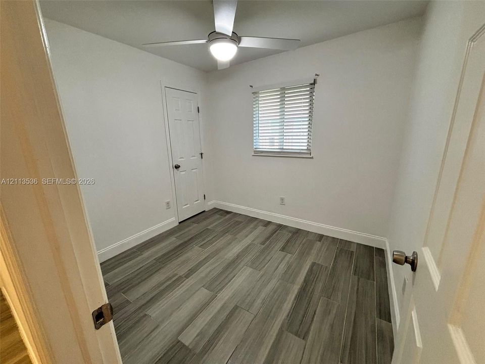 Room featuring wood-finish flooring, a ceiling-mounted light fixture with fan, and a single-panel interior door