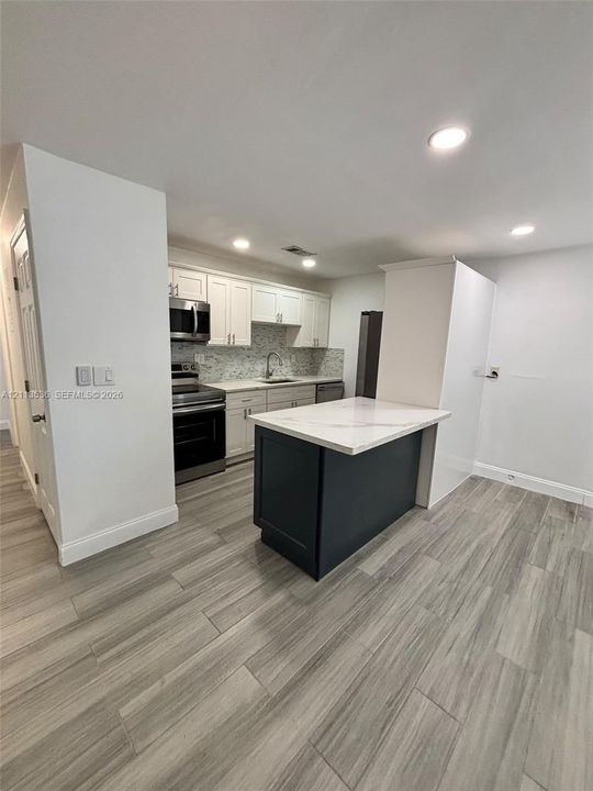 Kitchen featuring white cabinetry, stone-finish countertops, a contrasting dark-finish kitchen island, stainless steel appliances, and wood-finish flooring