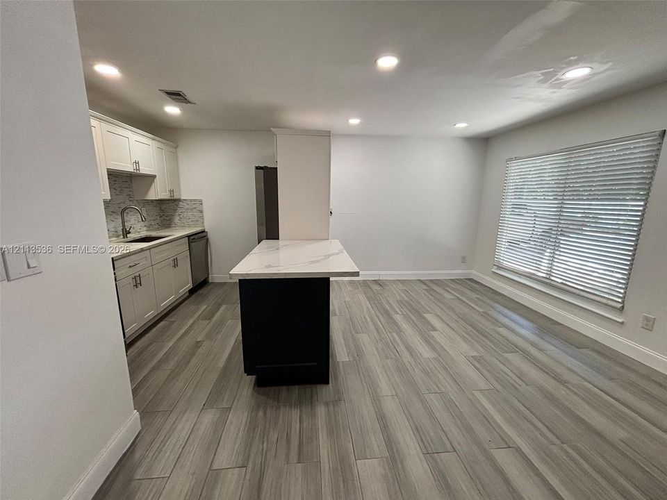Kitchen featuring white cabinetry, a contrasting dark central island with a stone-finish countertop, wood-finish flooring, recessed lighting, and a window with blinds
