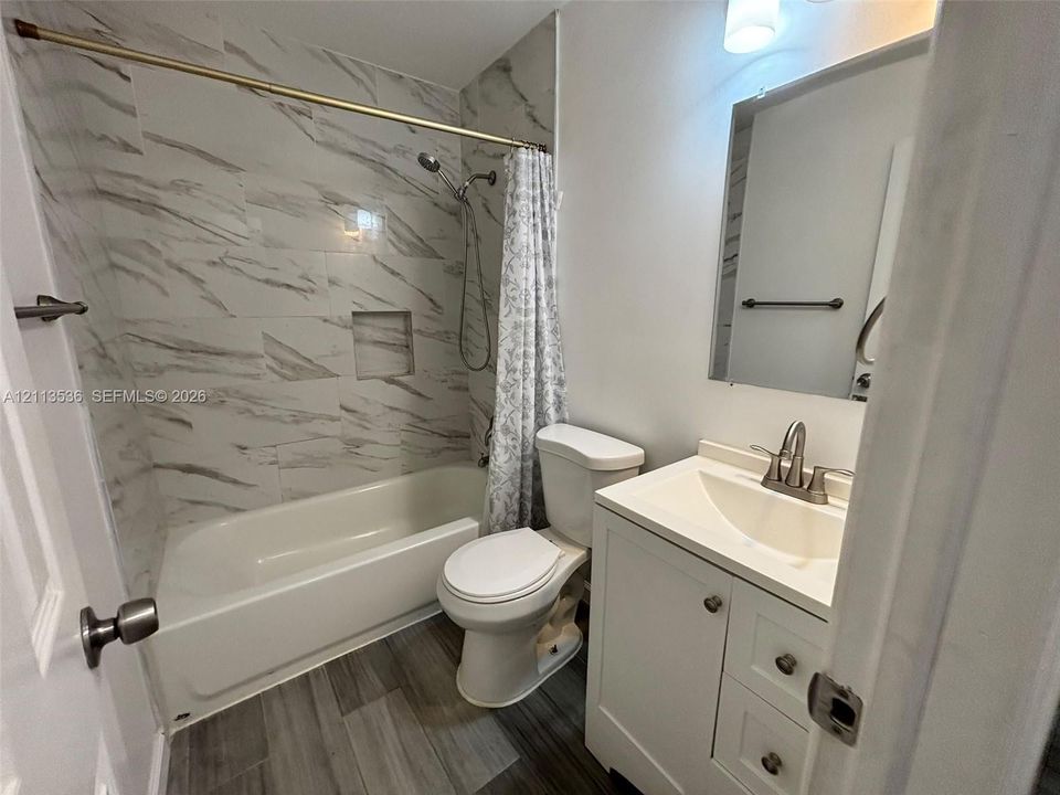 Bathroom featuring wood-finish flooring, white vanity with integrated basin, tub-shower combination with full-height stone-patterned tile surround, and built-in shower niche