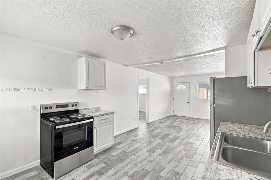 Kitchen featuring white cabinetry, stone-finish countertops, stainless steel appliances, and wood-finish tile flooring