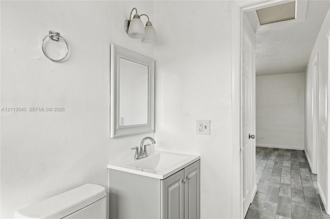 Vanity with neutral cabinetry and integrated sink, chrome-finish faucet, framed wall mirror, dual-light wall sconce, and wood-finish flooring